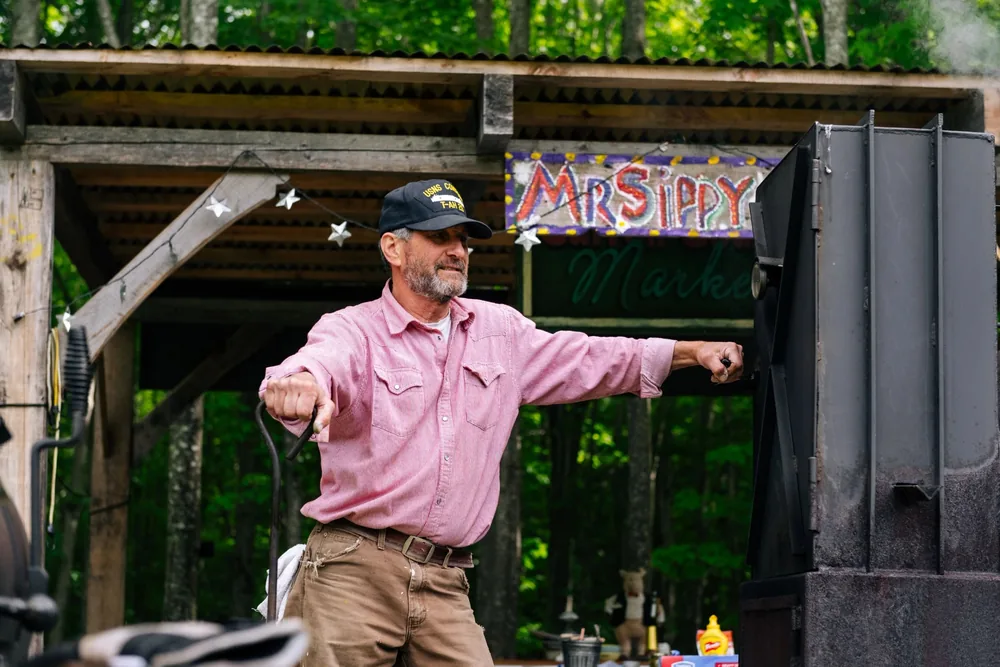 Cecil II, MrSippy himself, tending the fire on the smoker under the MrSippy Market sign