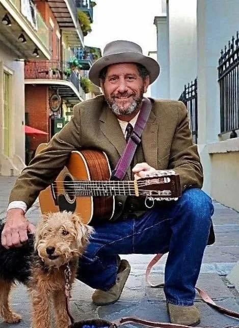 MrSippy crouched with his guitar and his dog Pie on a street in New Orleans