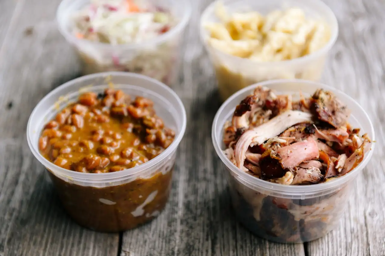 Pints of pulled pork, baked beans, slaw, and mac and cheese from MrSippy BBQ on a barnwood table