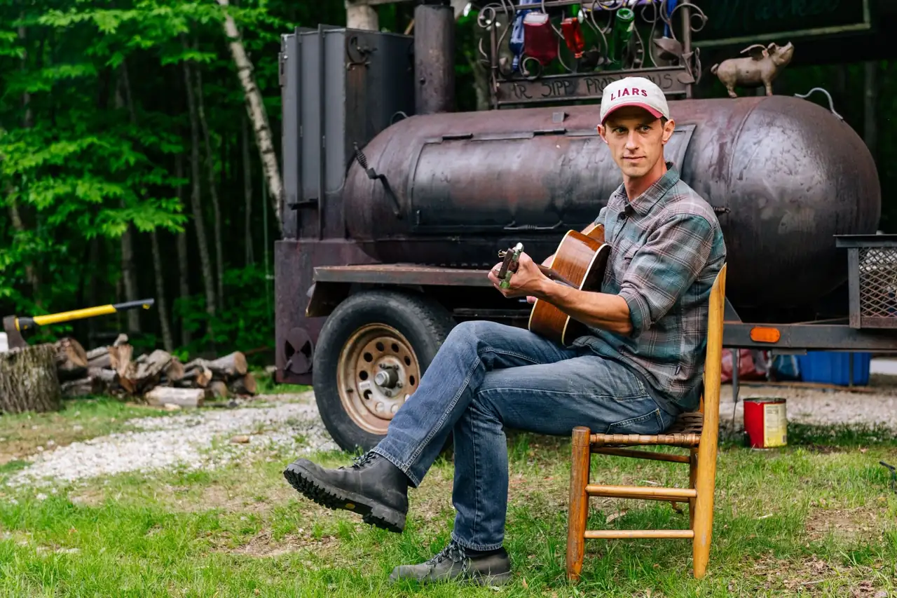 Cecil III picking an acoustic guitar in front of the Lang smoker