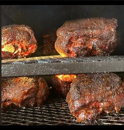 Pork butts with dark bark smoking over glowing coals